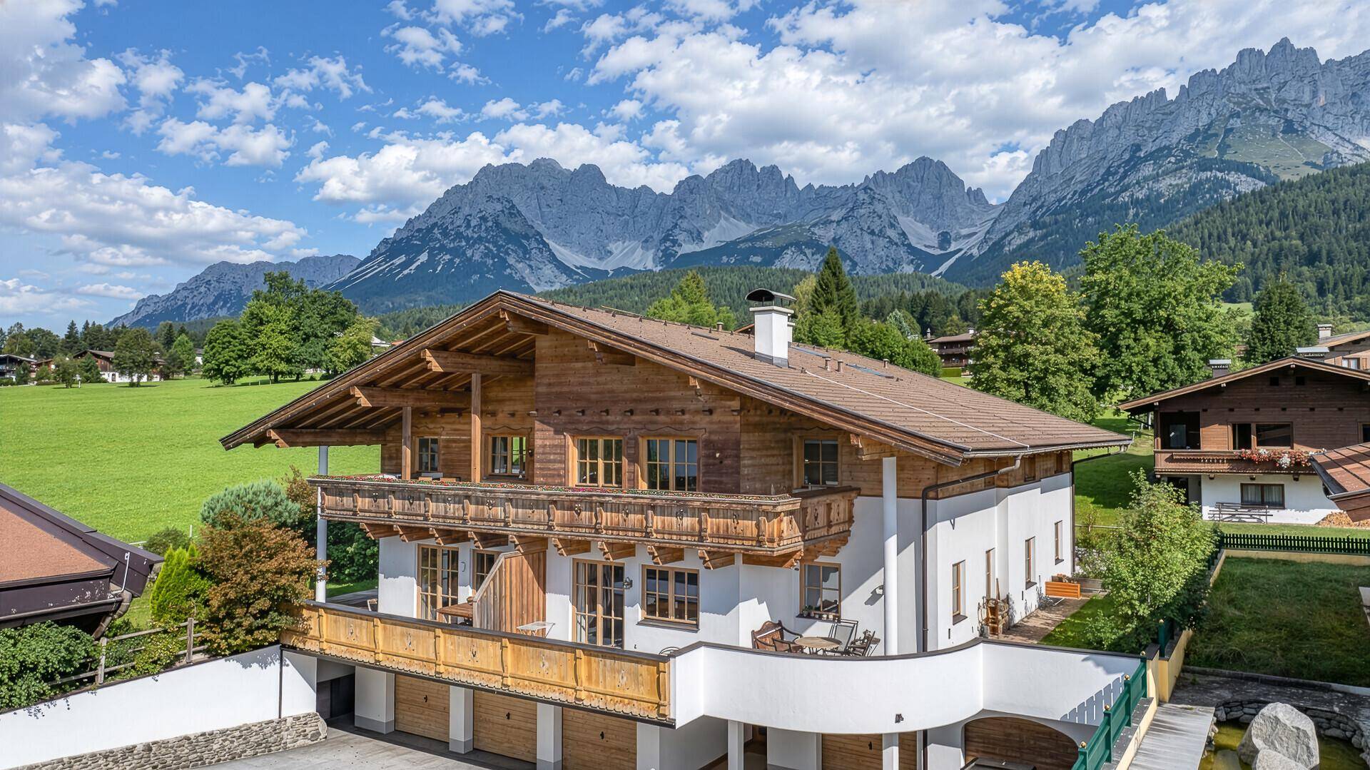 Großzügiges Alpenhaus mit mehreren Balkonen und integrierter Garage vor beeindruckender Berglandschaft.