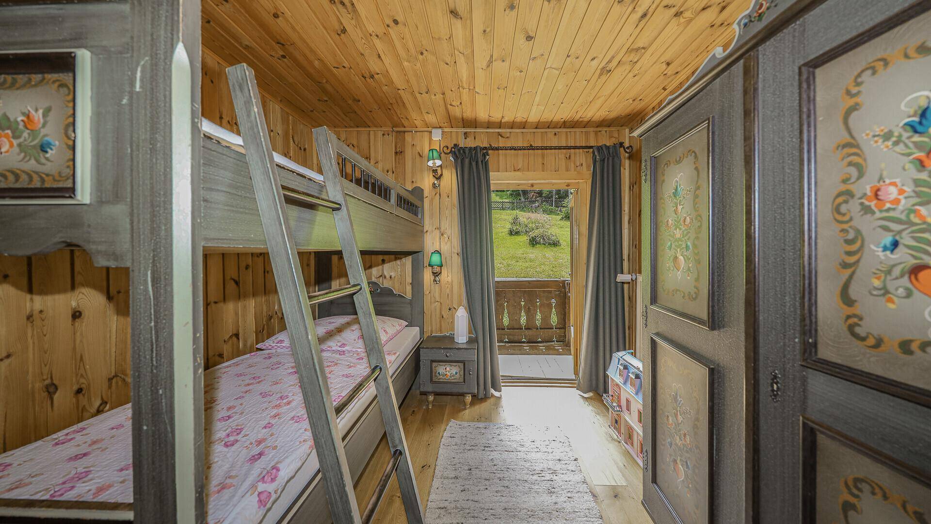 Kinderzimmer mit Etagenbetten, Holzvertäfelung und Zugang zu einem kleinen Balkon mit Blick ins Grüne.