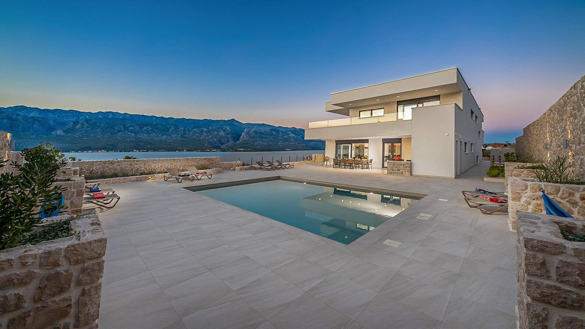 Ruhiger Poolbereich der Villa bei Sonnenuntergang, umgeben von Steinmauern und mit Meerblick.
