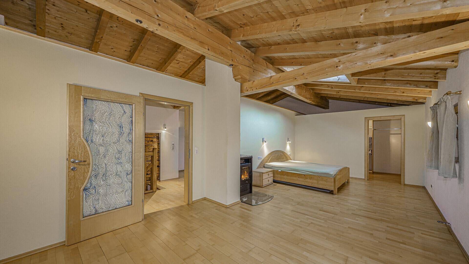 Gemütliches Schlafzimmer im Dachgeschoss mit Holzbalkendecke, Holzfußboden und einem kleinen Kaminofen.