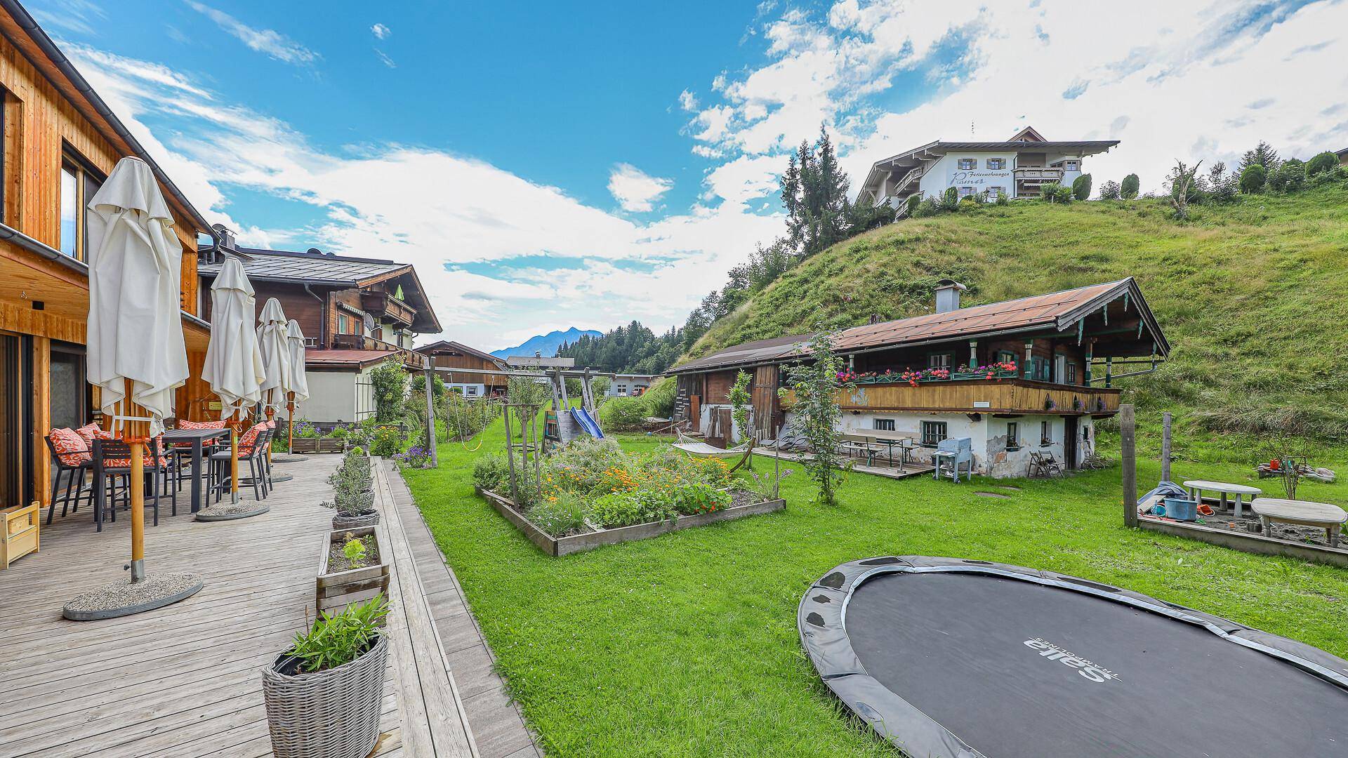 Weitläufiger Garten mit Rasenfläche, Trampolin und angrenzender Holzterrasse.