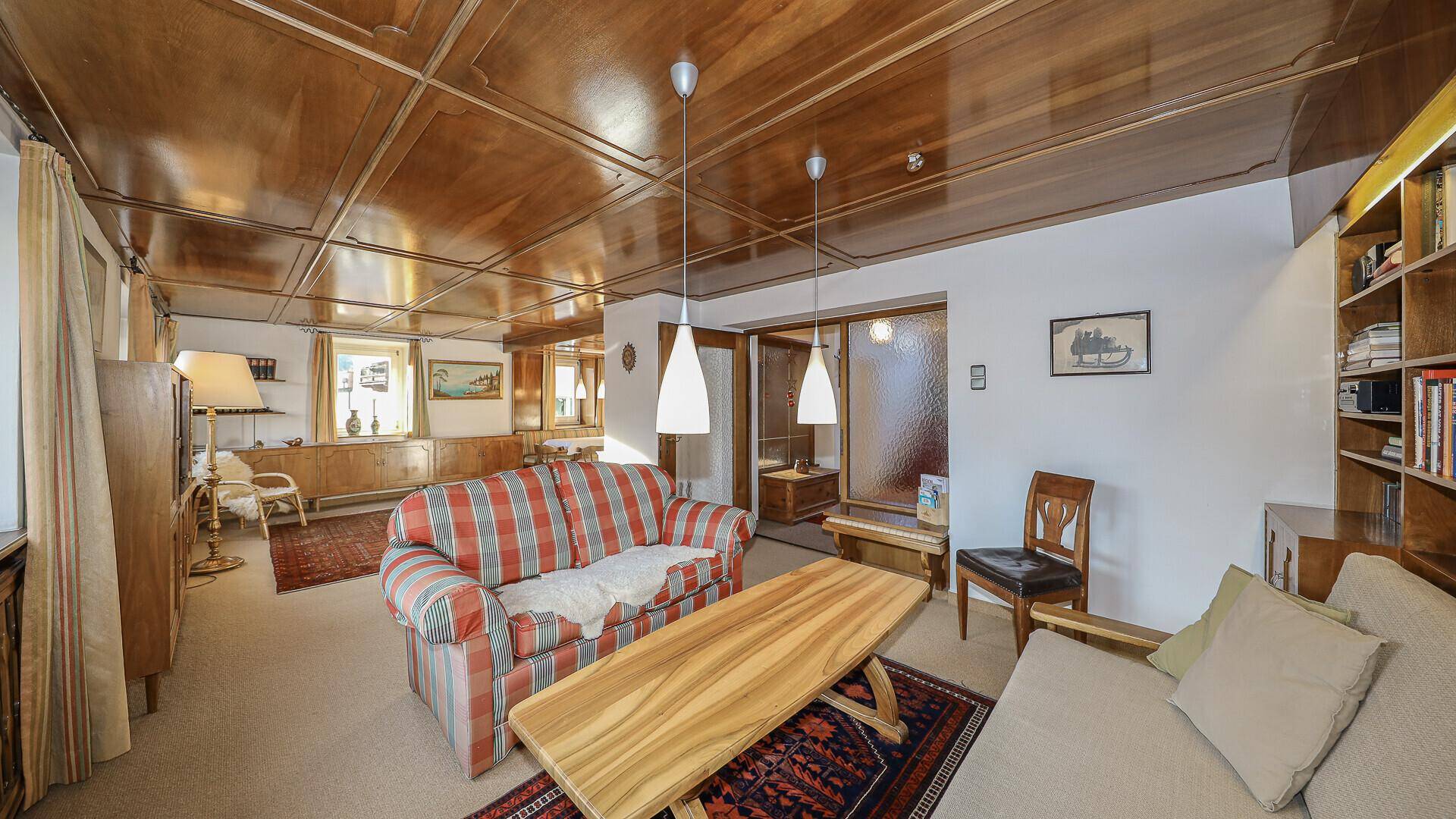 Heller Wohnbereich mit Holzdecke, bequemen Sofas und einem traditionellen Teppich.