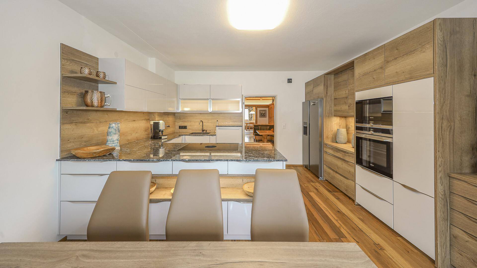 Helle, moderne Küche mit Essbereich, ausgestattet mit eleganten Holz- und weißen Schränken und Holzboden.