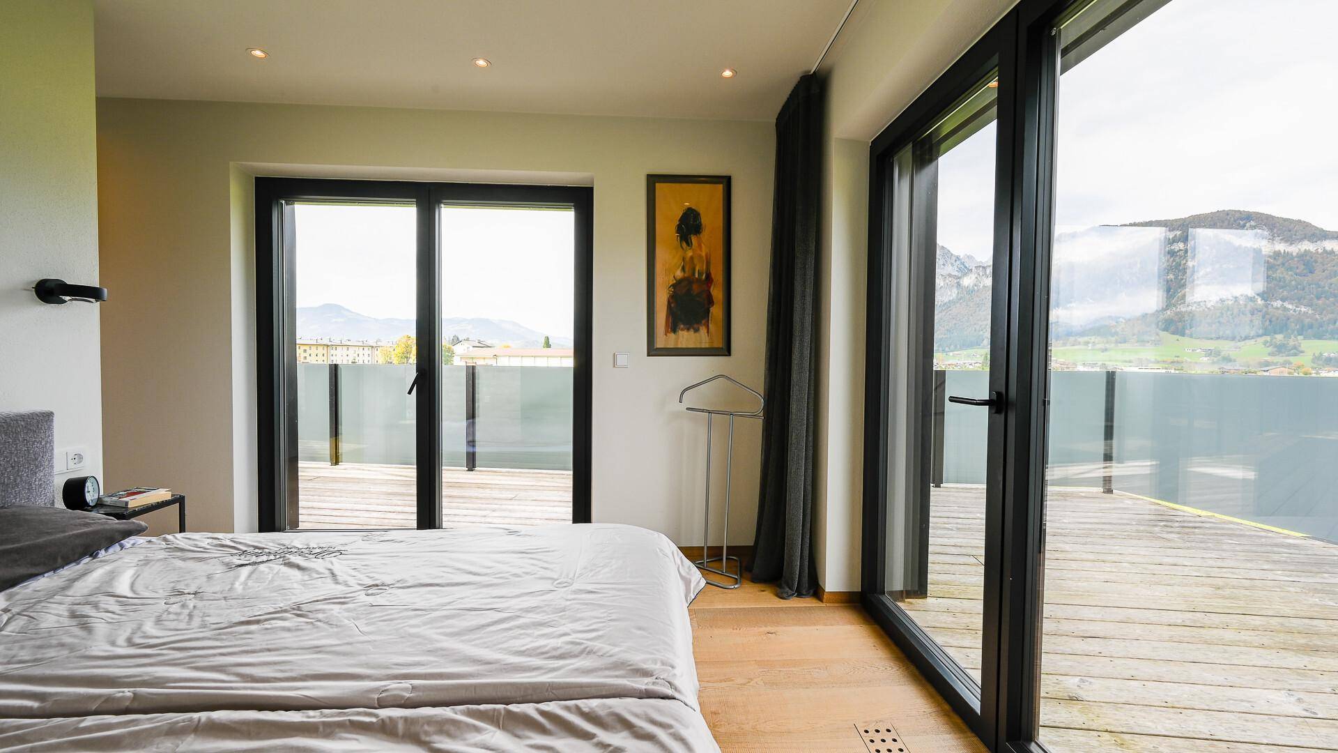 Helles Schlafzimmer mit Holzboden und großen Fenstern, die einen weiten Blick auf die Landschaft bieten.