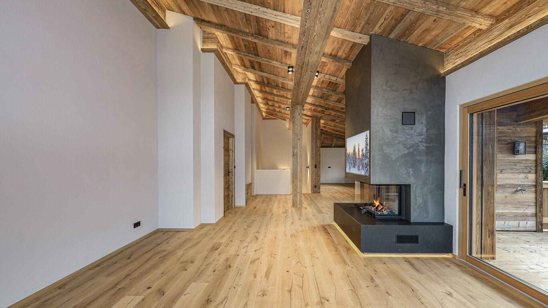 Weitläufiger Wohnbereich mit Holzbalkendecke, Kamin und hellem Holzboden, der viel Platz bietet.