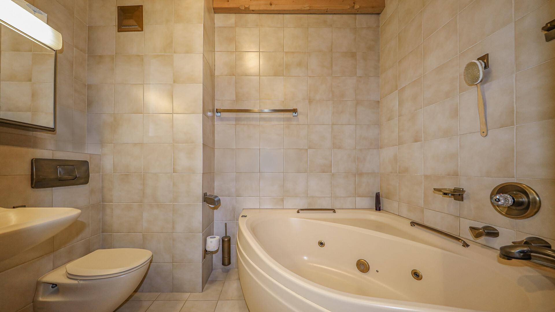 Funktionales Badezimmer mit Eckbadewanne, WC und hellen beigefarbenen Fliesen.
