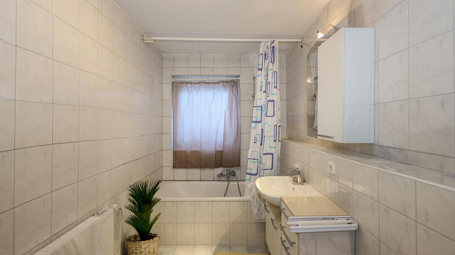 Helles Badezimmer mit Badewanne, Waschbecken und Fliesen, funktional und einfach ausgestattet.