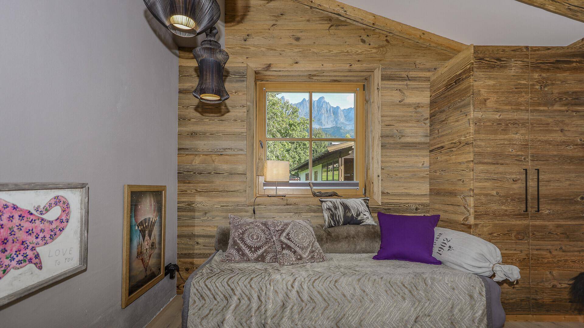 Schlafzimmer mit Holzwänden, Tagesbett und Fenster mit Blick auf die umliegende Landschaft.