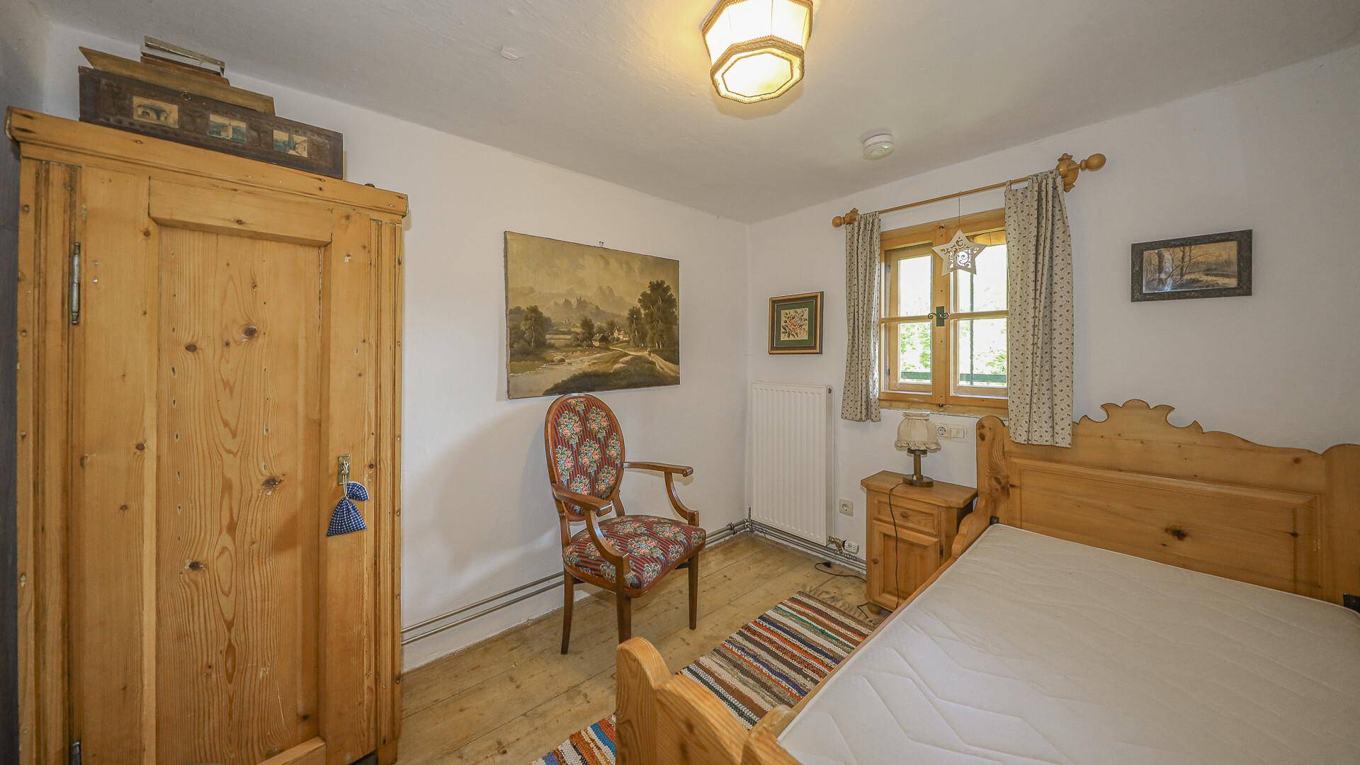 Helles Schlafzimmer mit Holzbett, traditionellem Kleiderschrank und Blick ins Grüne.