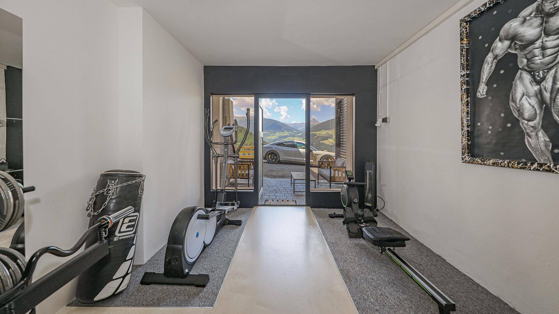 Fitnessraum mit Trainingsgeräten und Zugang zu einem Außenbereich mit Bergblick.