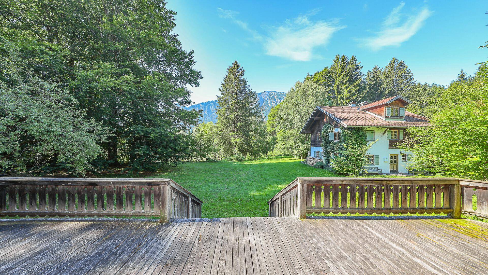 Große Holzterrasse mit Blick auf den weitläufigen Garten und die umliegenden Berge.