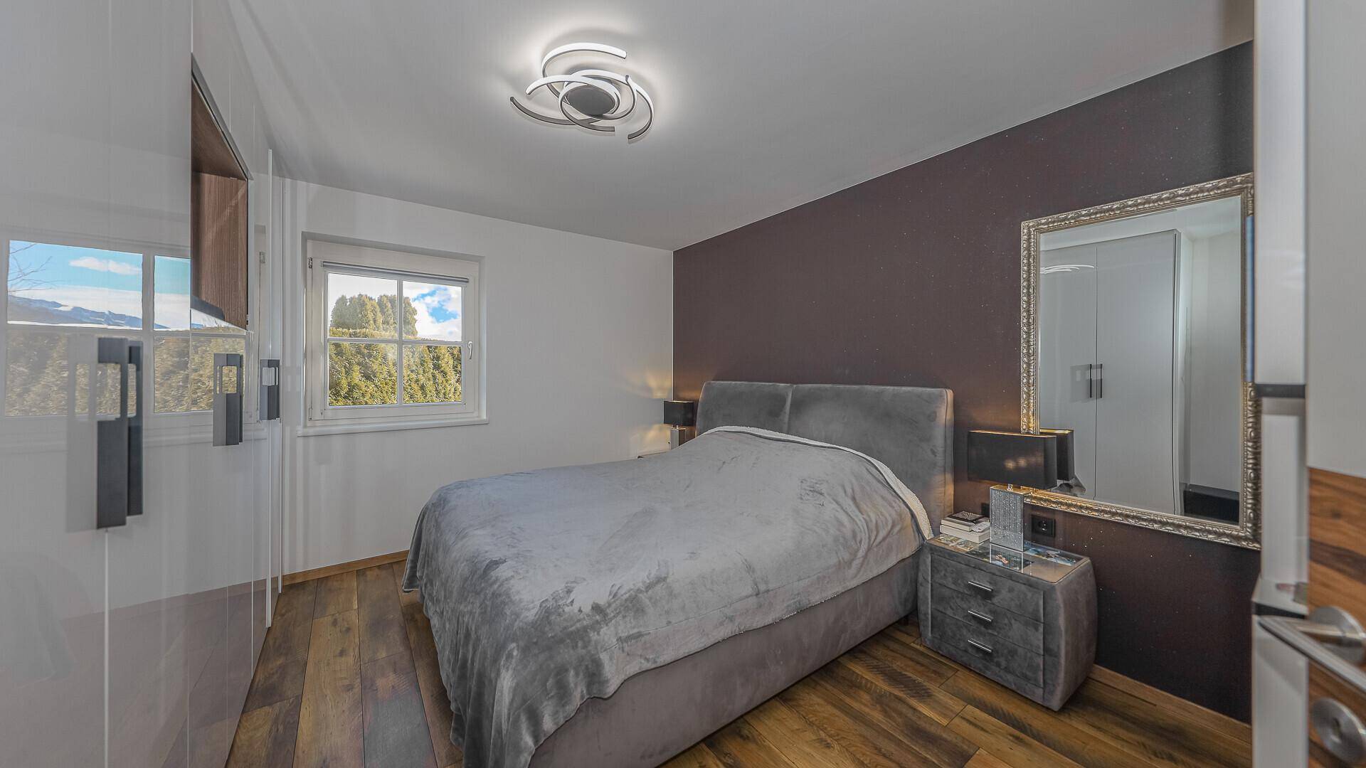Gemütliches Schlafzimmer mit modernem Bett, Einbauschränken und Blick ins Grüne durch das Fenster.