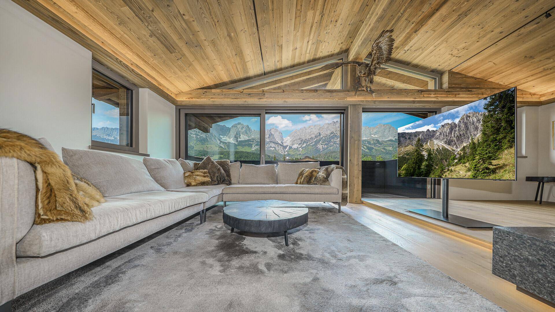 Helles Wohnzimmer mit Panoramablick auf die Berge, Holzbalkendecke und großem Sofa.