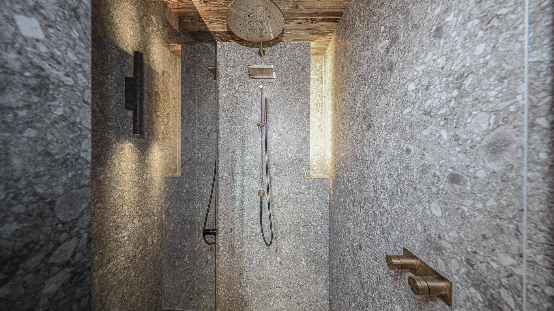 Elegante Duschkabine mit Regendusche und Steinoptik-Fliesen an Wänden und Boden.