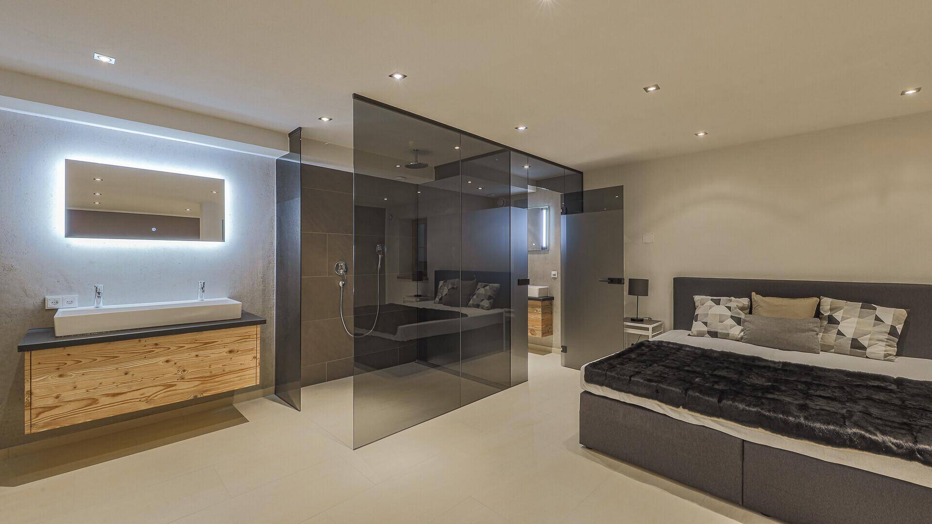 Großzügiges Schlafzimmer mit offenem Badbereich, Waschtisch und moderner Glasdusche.