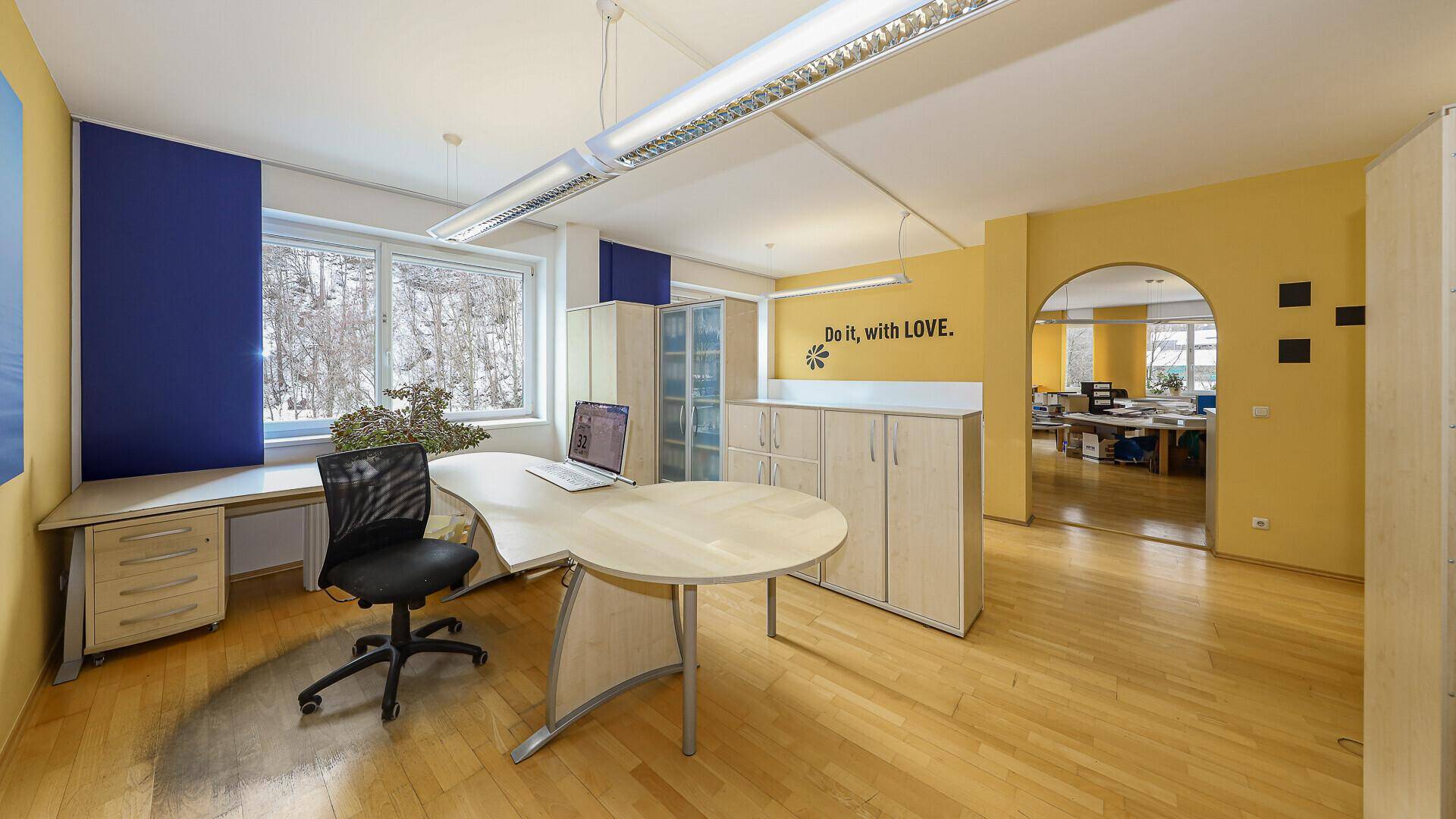 Großes Büro mit Holzboden, gelben Wänden und einem Durchgang zu weiteren Räumen, hell und funktional.