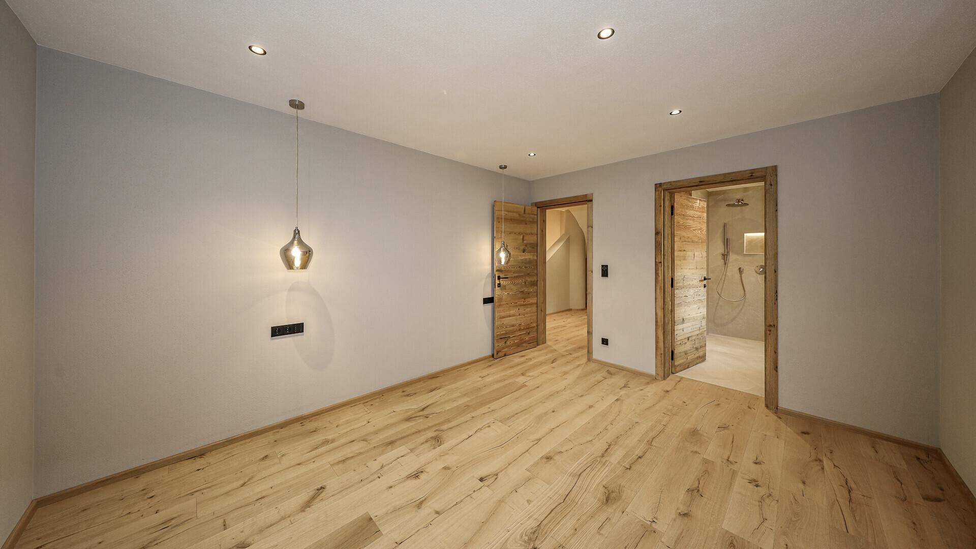 Geräumiges Schlafzimmer mit Holzboden und Zugang zu weiteren Räumen, darunter ein Badezimmer.