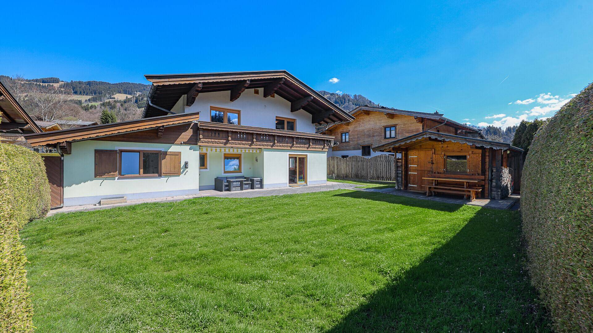 Großer, gepflegter Gartenbereich mit Rasenfläche, Gartenhaus und Bergblick.