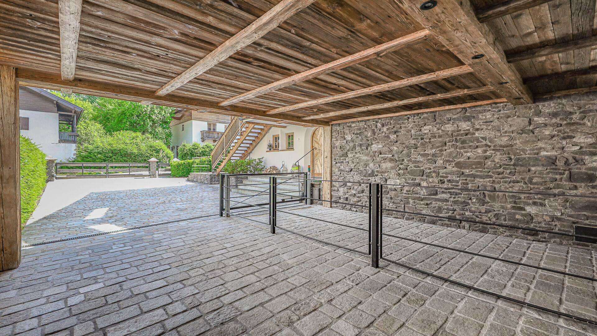 Überdachter Parkplatz mit Steinmauer und gepflasterter Einfahrt zum Chalet.