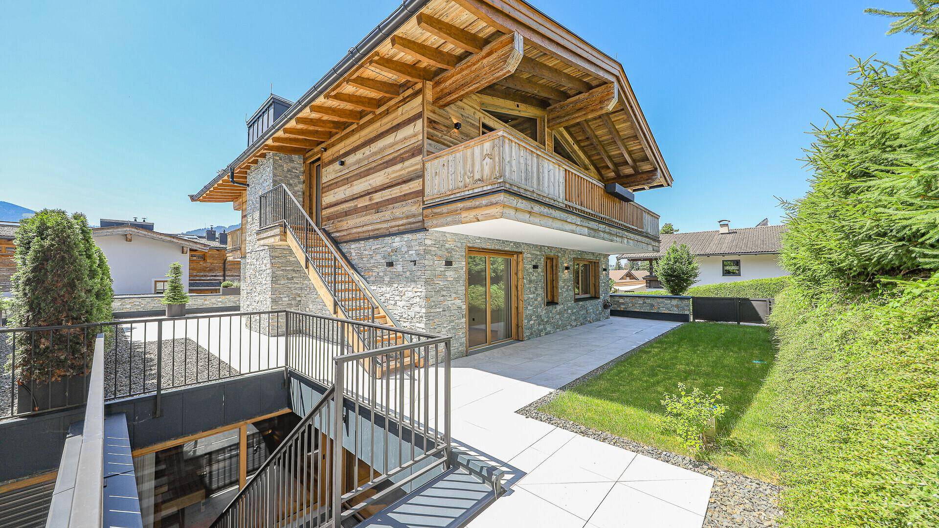 Außenbereich mit Rasenfläche, gepflasterter Terrasse und Treppe zum oberen Balkon.
