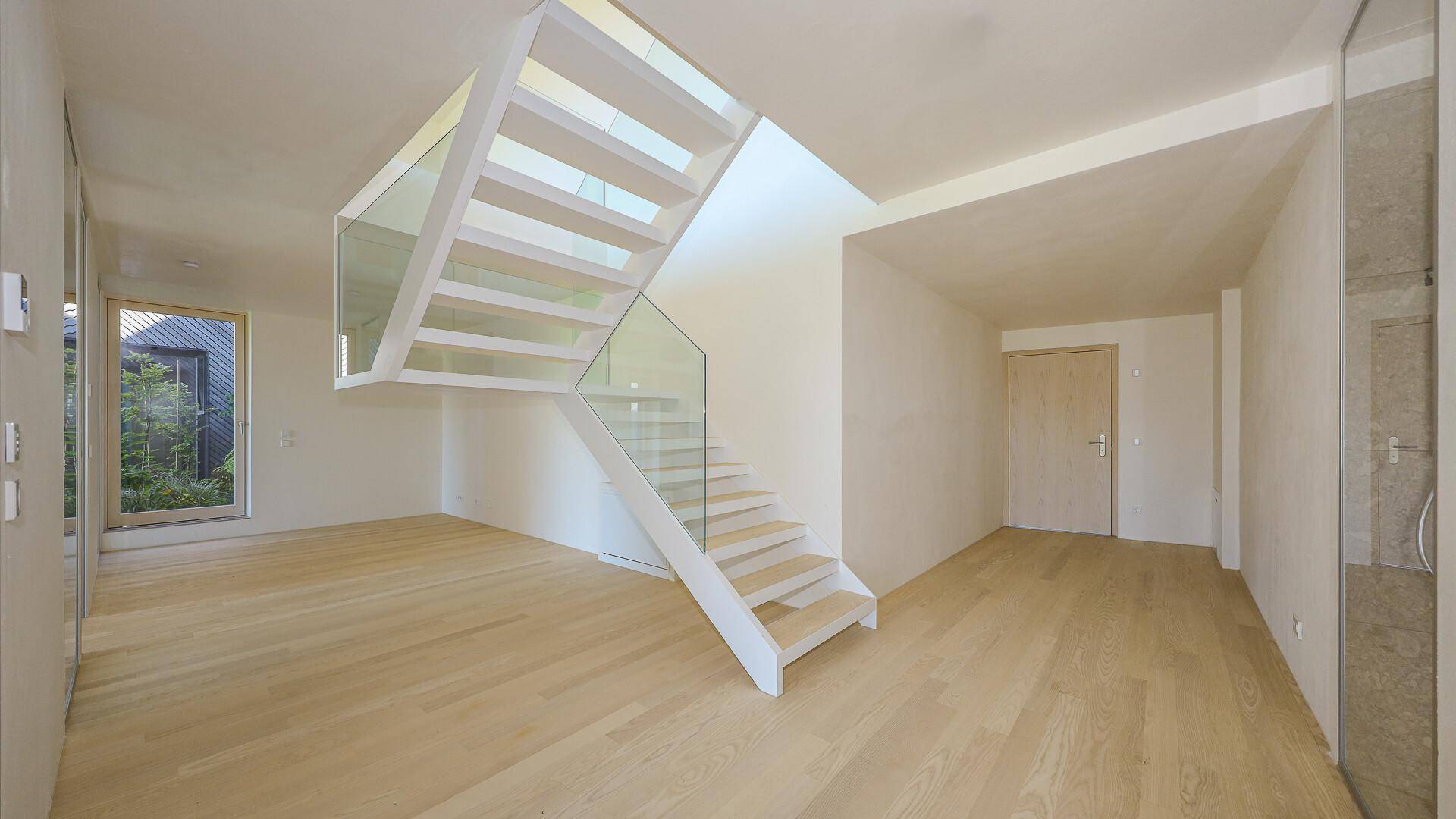 Heller Flurbereich mit moderner Treppe aus Holz und Glasgeländer.