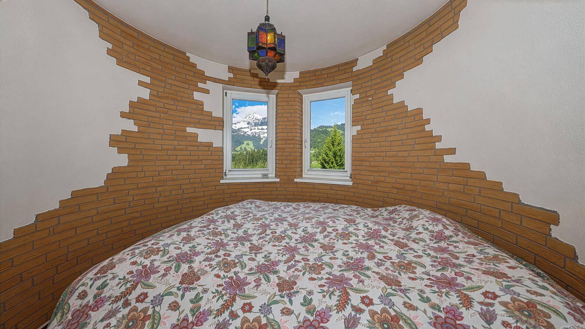 Schlafzimmer mit Doppelbett, Ziegelakzenten an den Wänden und Bergblick.