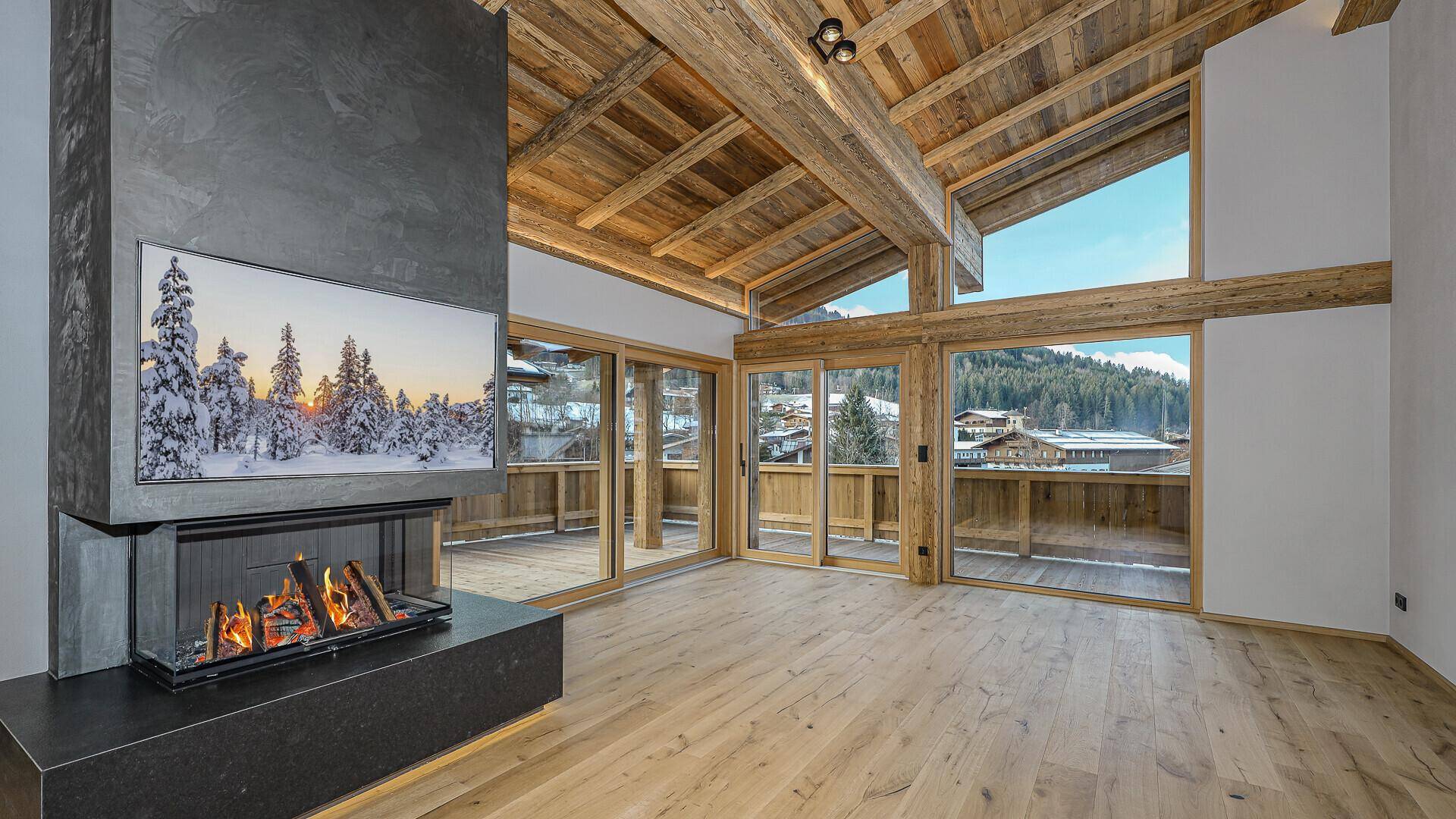Geräumiges Wohnzimmer mit modernem Kamin, Holzbalkendecke und großen Fenstern mit Bergblick.