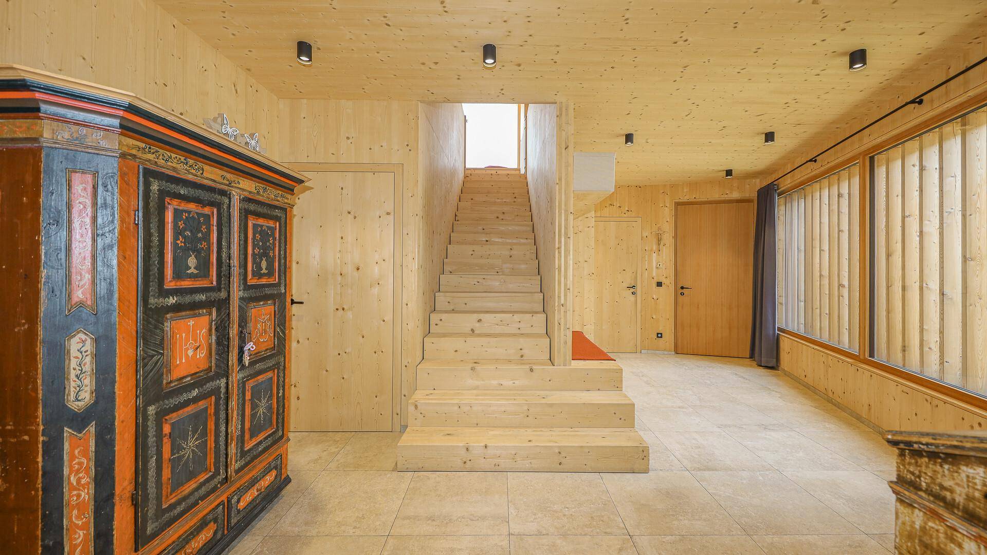Heller Eingangsbereich mit Holztreppe, Fliesenboden und einem traditionellen bemalten Schrank.