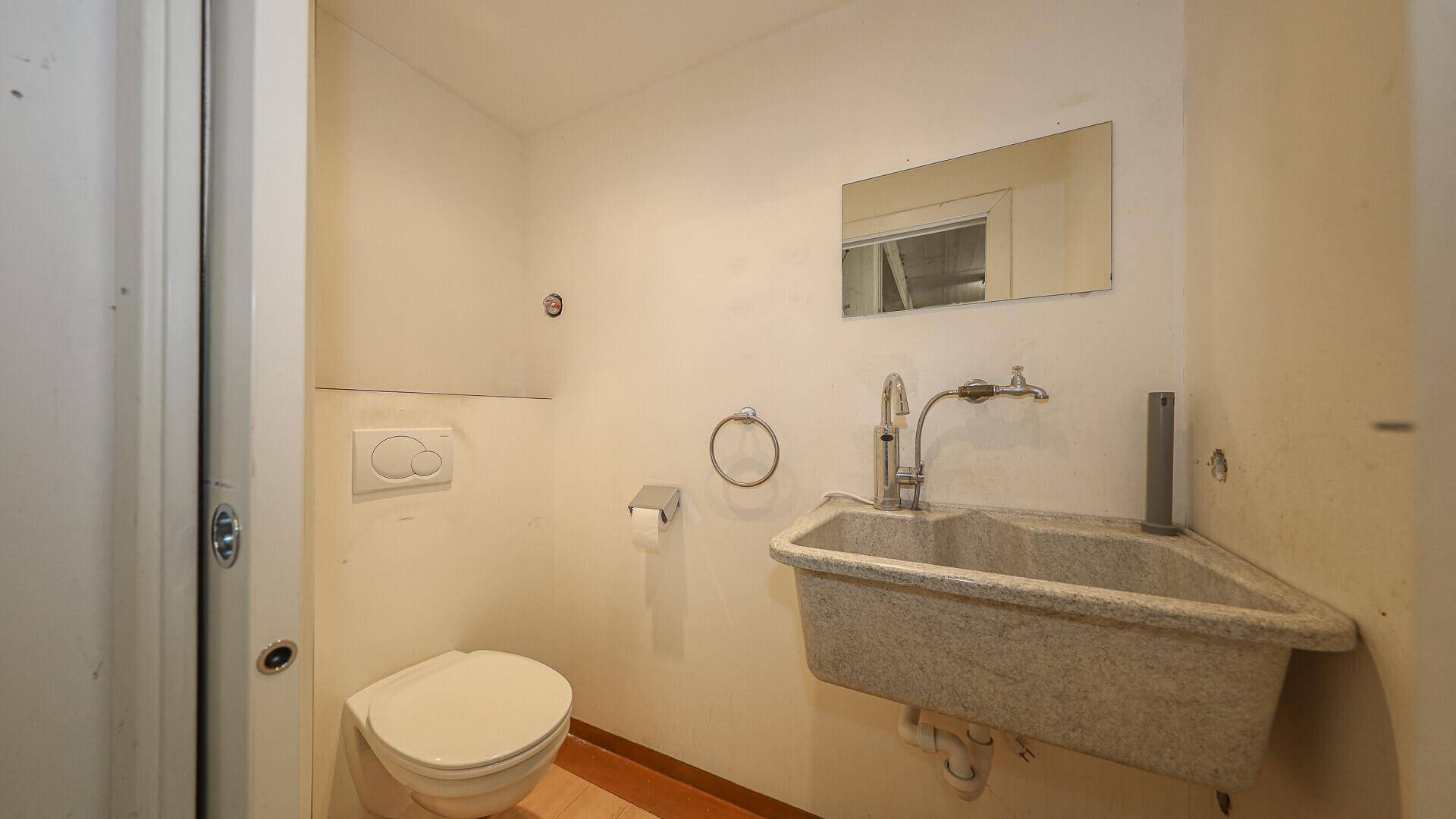 Kleines Badezimmer mit Toilette, Waschbecken und einem Spiegel, funktional und einfach ausgestattet.