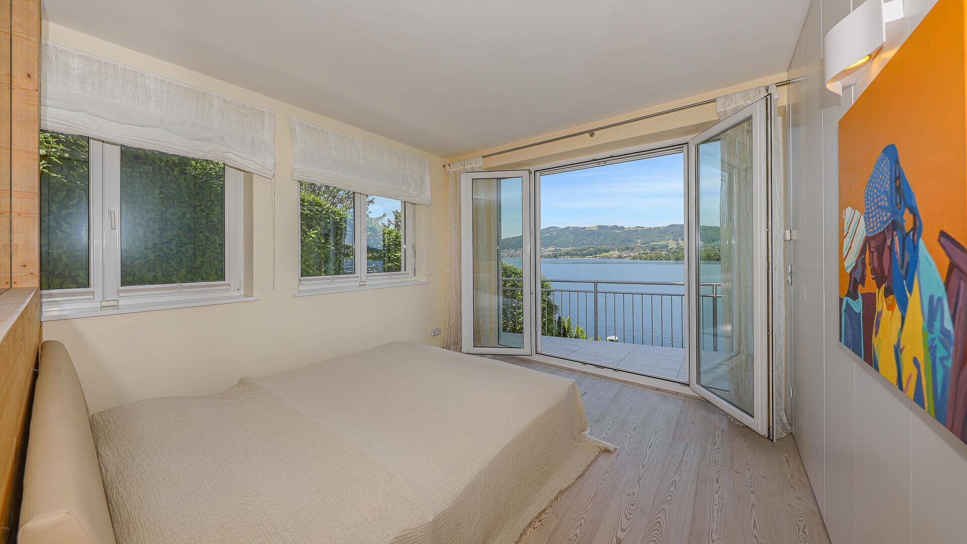 Helles Schlafzimmer mit Holzboden, Einbauschränken und Zugang zum Balkon mit Seeblick.