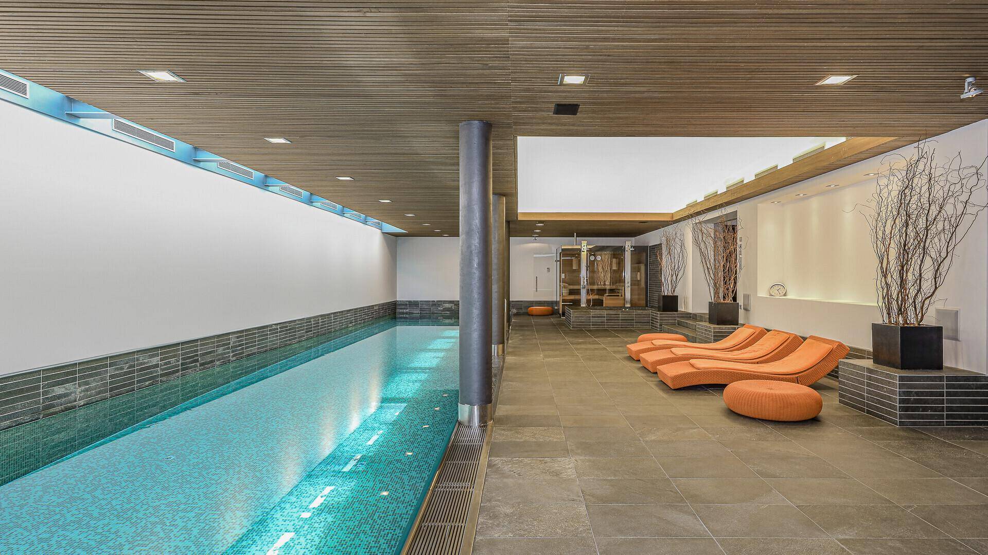 Exklusiver Wellnessbereich mit langem Innenpool, Liegestühlen und stilvoller Beleuchtung.