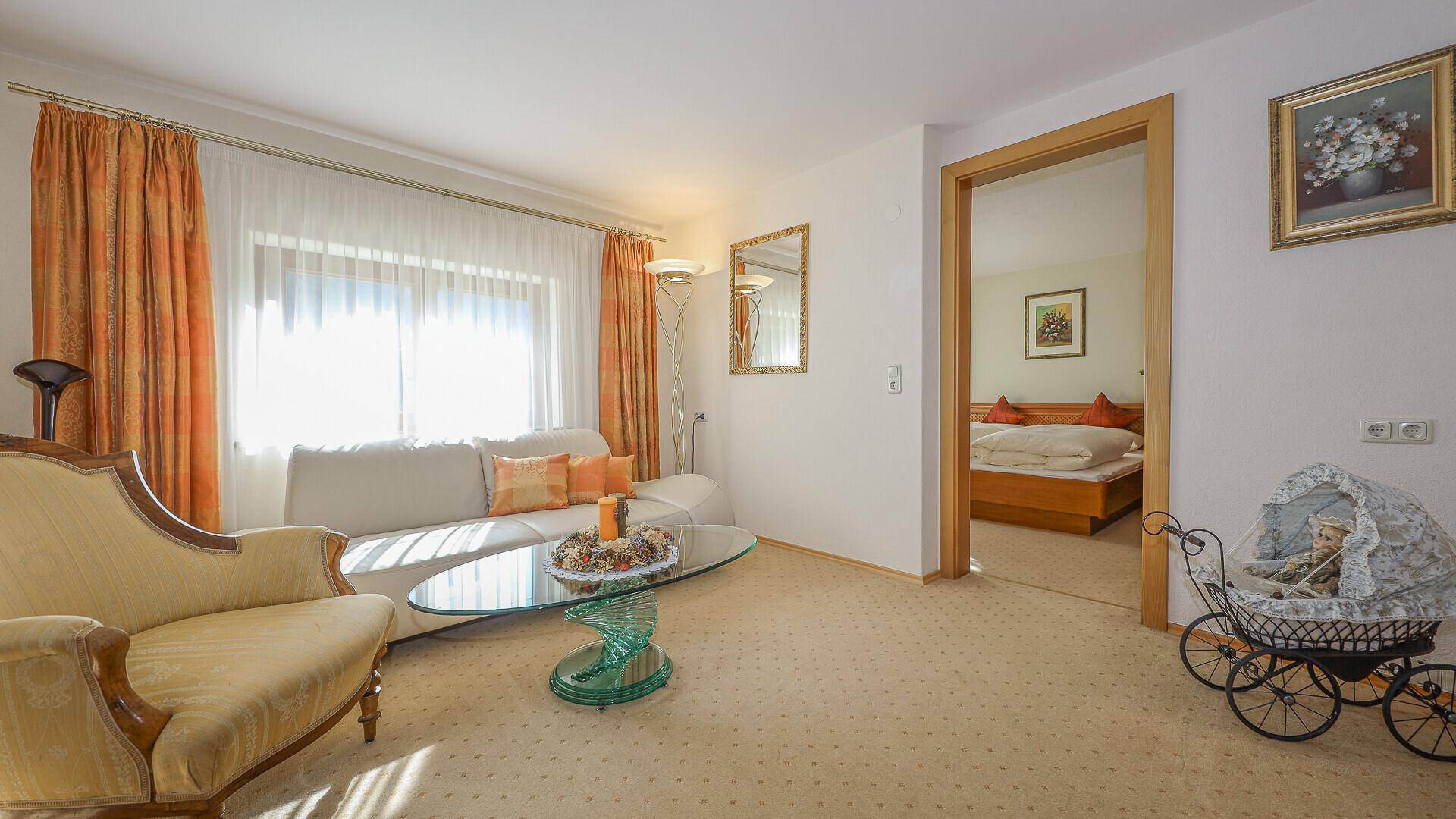 Helles Wohnzimmer mit Sofa, Teppichboden und Zugang zu einem weiteren Zimmer.