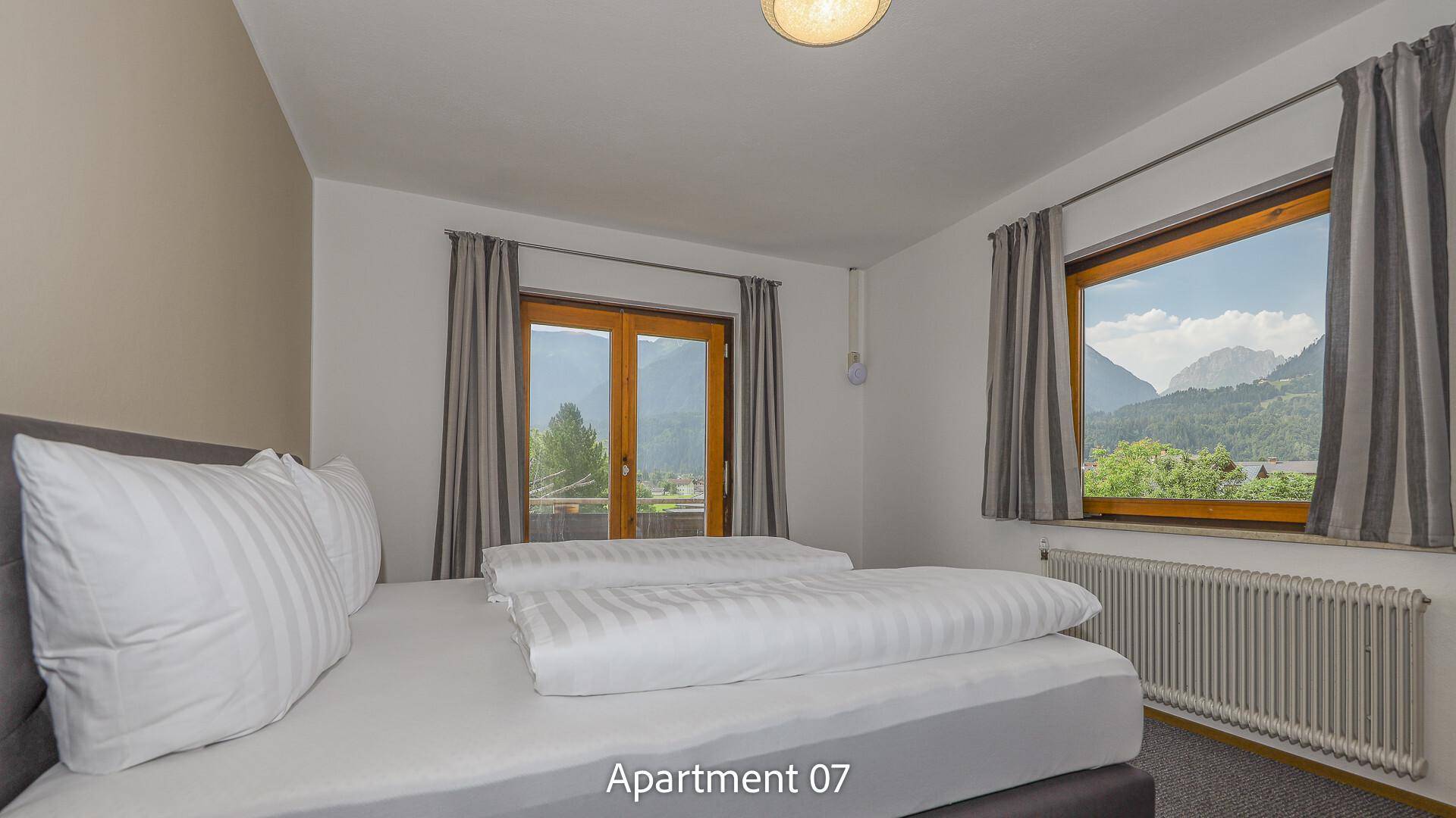 Schlafzimmer von Apartment 07 mit Doppelbett, Nachttischen und Fenstern mit Bergblick.