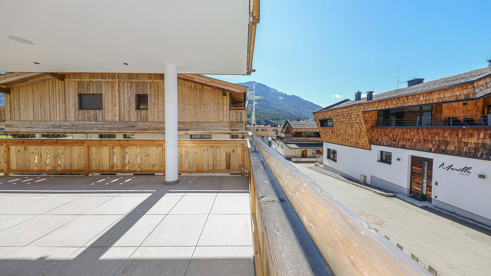 Sonniger Balkon mit traditionellen Holzelementen und Blick auf die Straße und Berge.