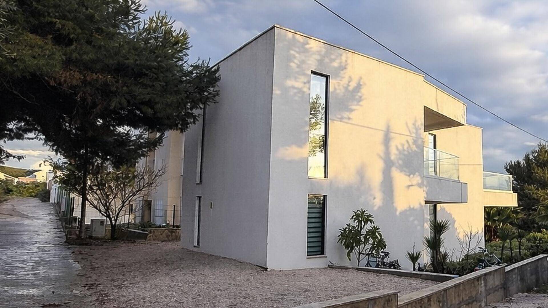 Moderne Villa mit minimalistischer Architektur, großen Fenstern und natürlicher Umgebung bei Sonnenuntergang.