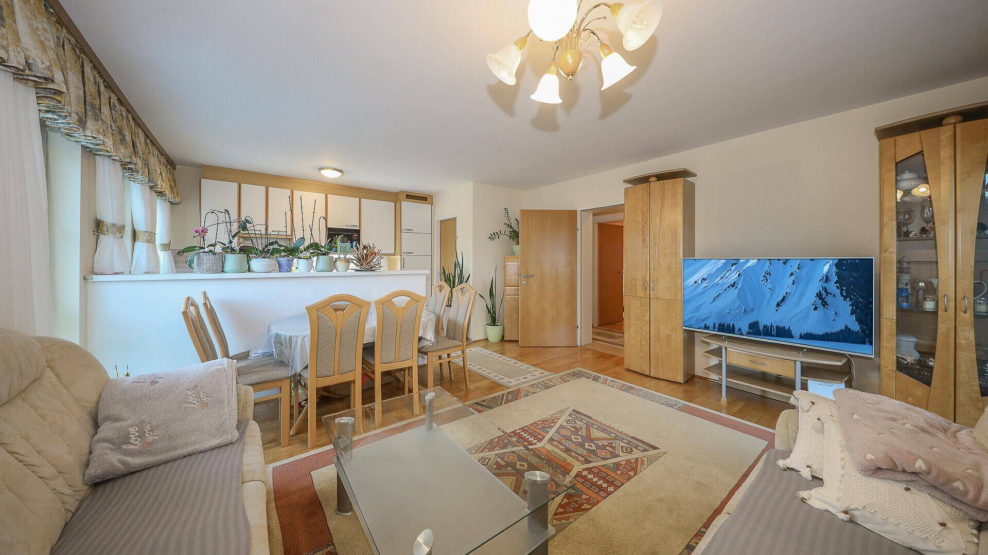 Heller Wohn-Essbereich mit Fernseher und Blick auf die halb offene Küche, gemütlich eingerichtet.