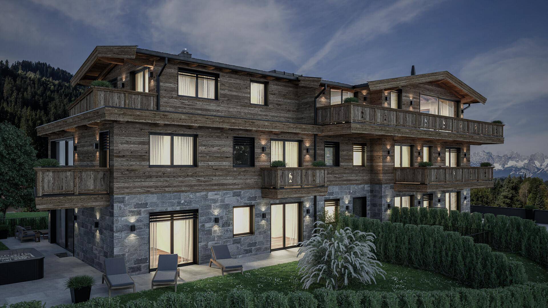 Beleuchtetes Chalet bei Nacht mit Holzfassade, Steinsockel und Whirlpool mit Bergblick.