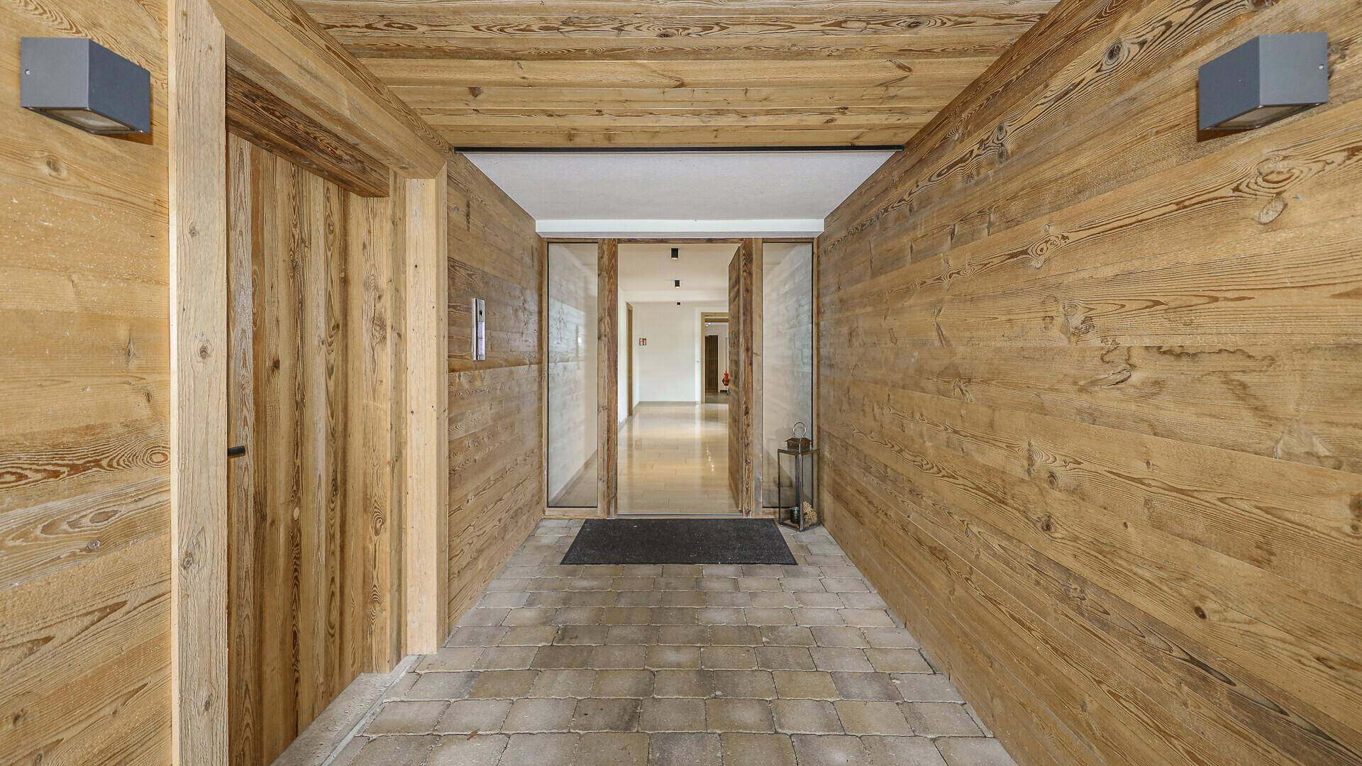 Eingangsbereich mit rustikalen Holzverkleidungen an Wänden und Decke sowie Fliesenboden.