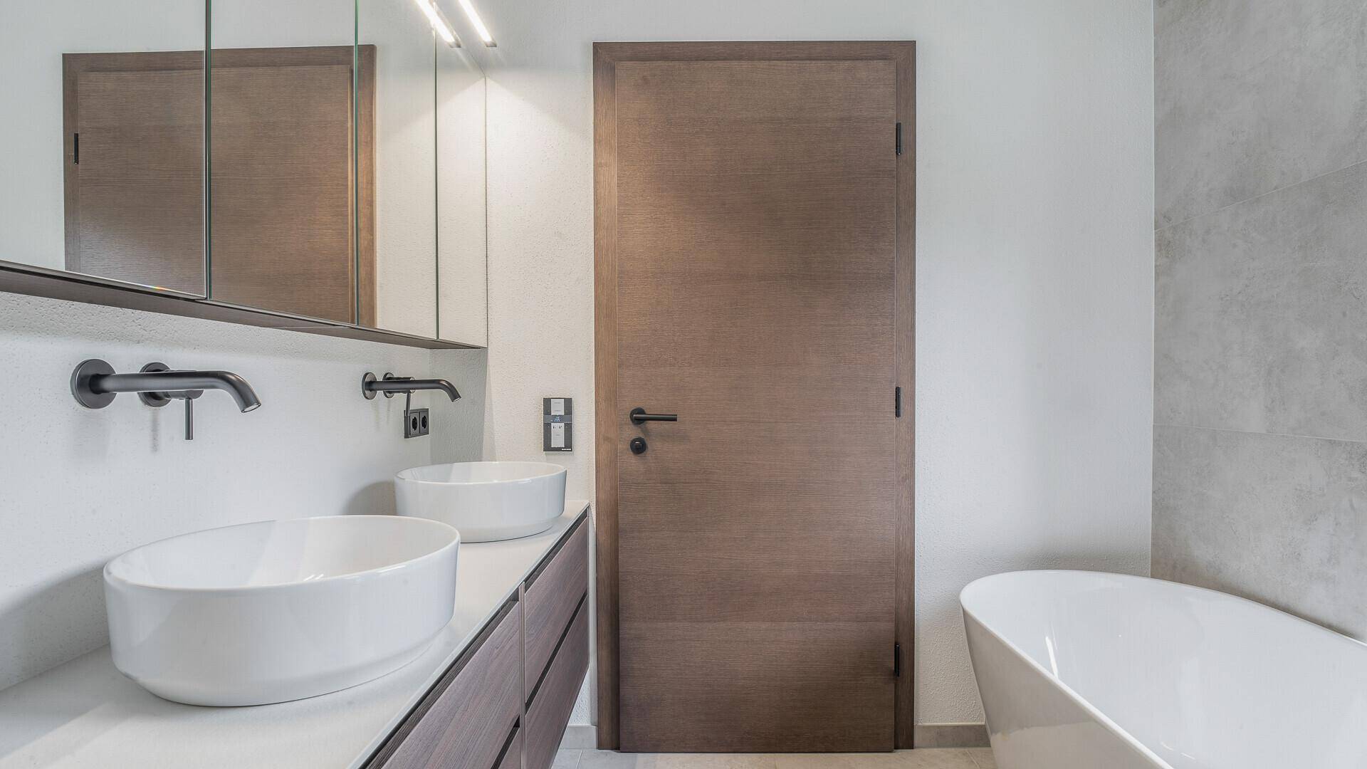 Modernes Badezimmer mit Doppelwaschbecken, Badewanne und eleganten dunklen Armaturen.