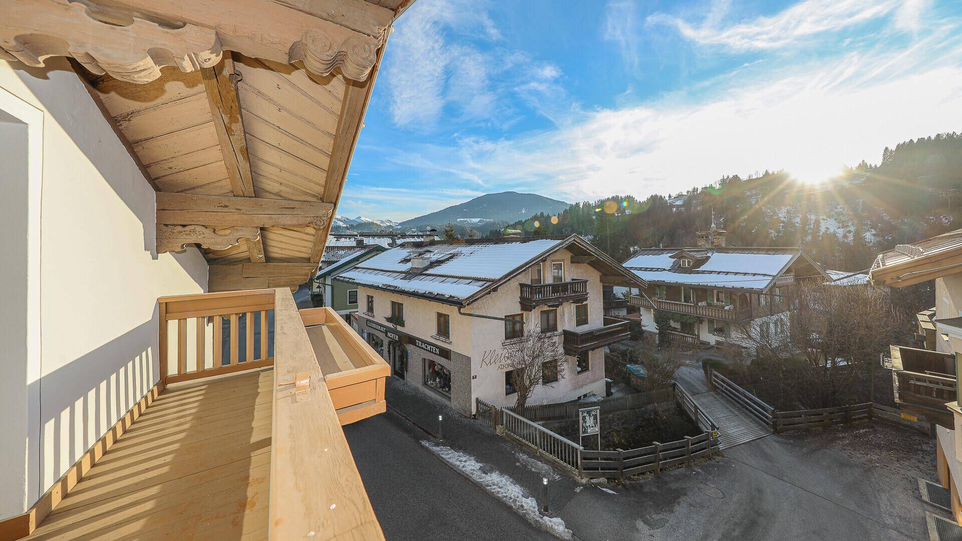 Sonniger Holzbalkon mit weitem Blick über das Dorf und die schneebedeckten Berge.