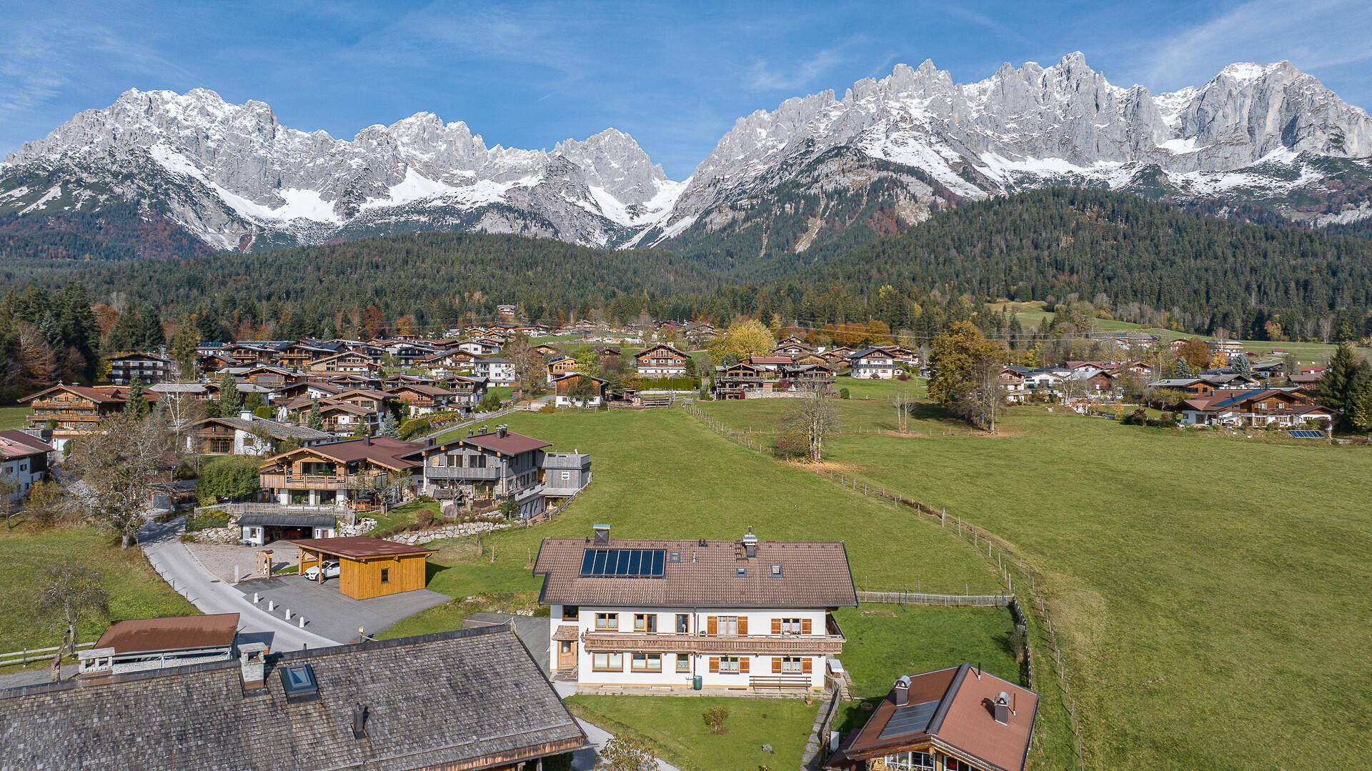 Luftaufnahme eines traditionellen Hauses mit Solaranlage und beeindruckendem Alpenpanorama.