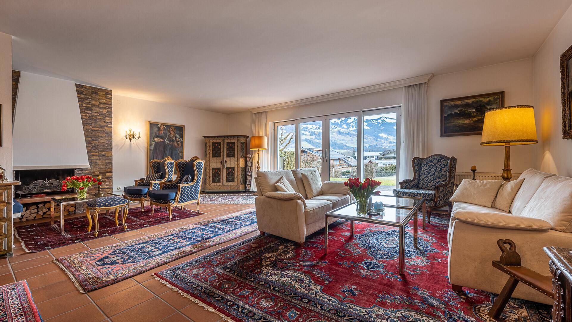 Geräumiges Wohnzimmer mit Kamin, bequemen Sofas und weitem Blick auf die winterliche Bergkulisse.