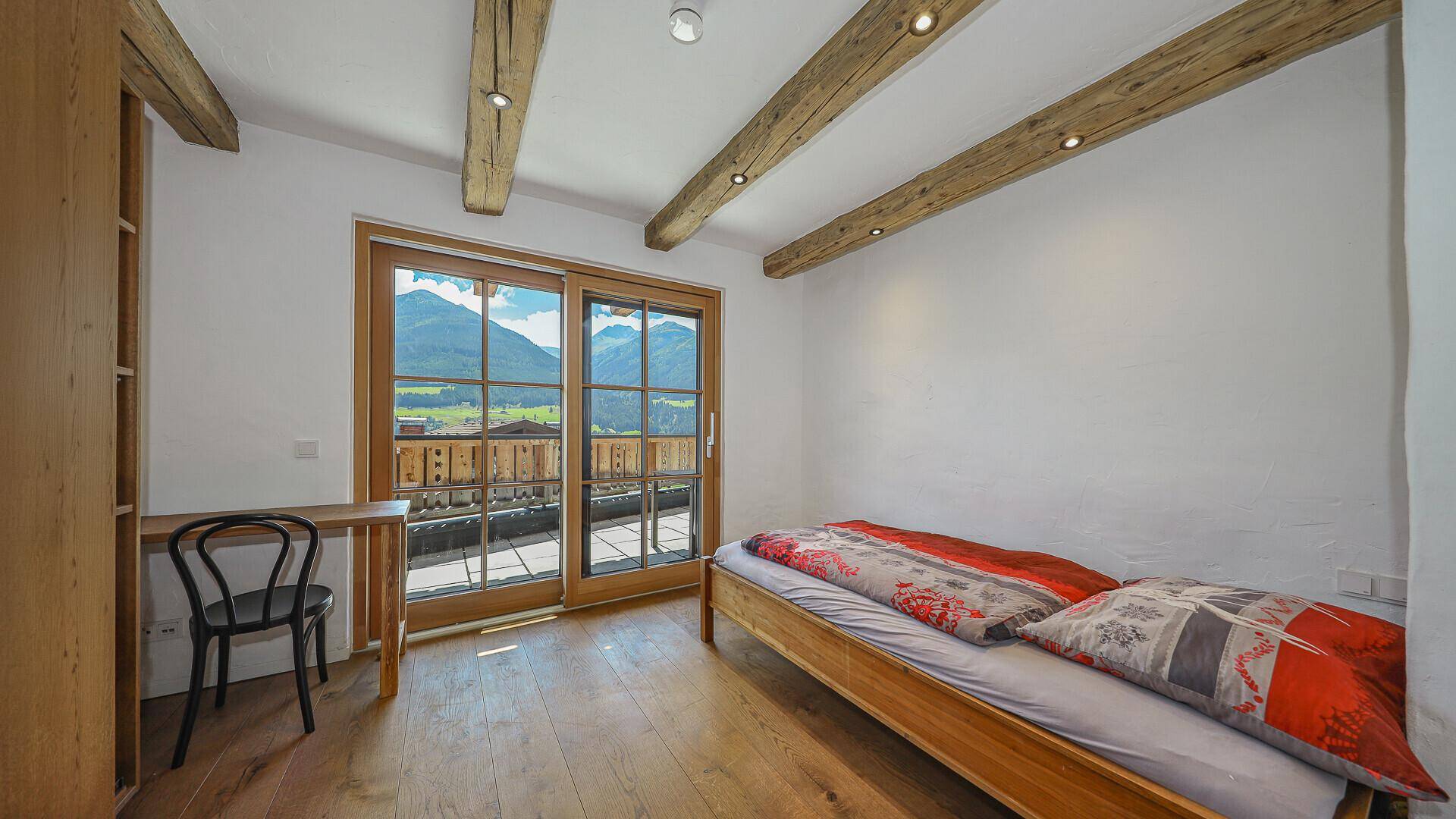 Schlafzimmer mit Holzbalken, Parkettboden und großen Fenstern mit Bergblick.