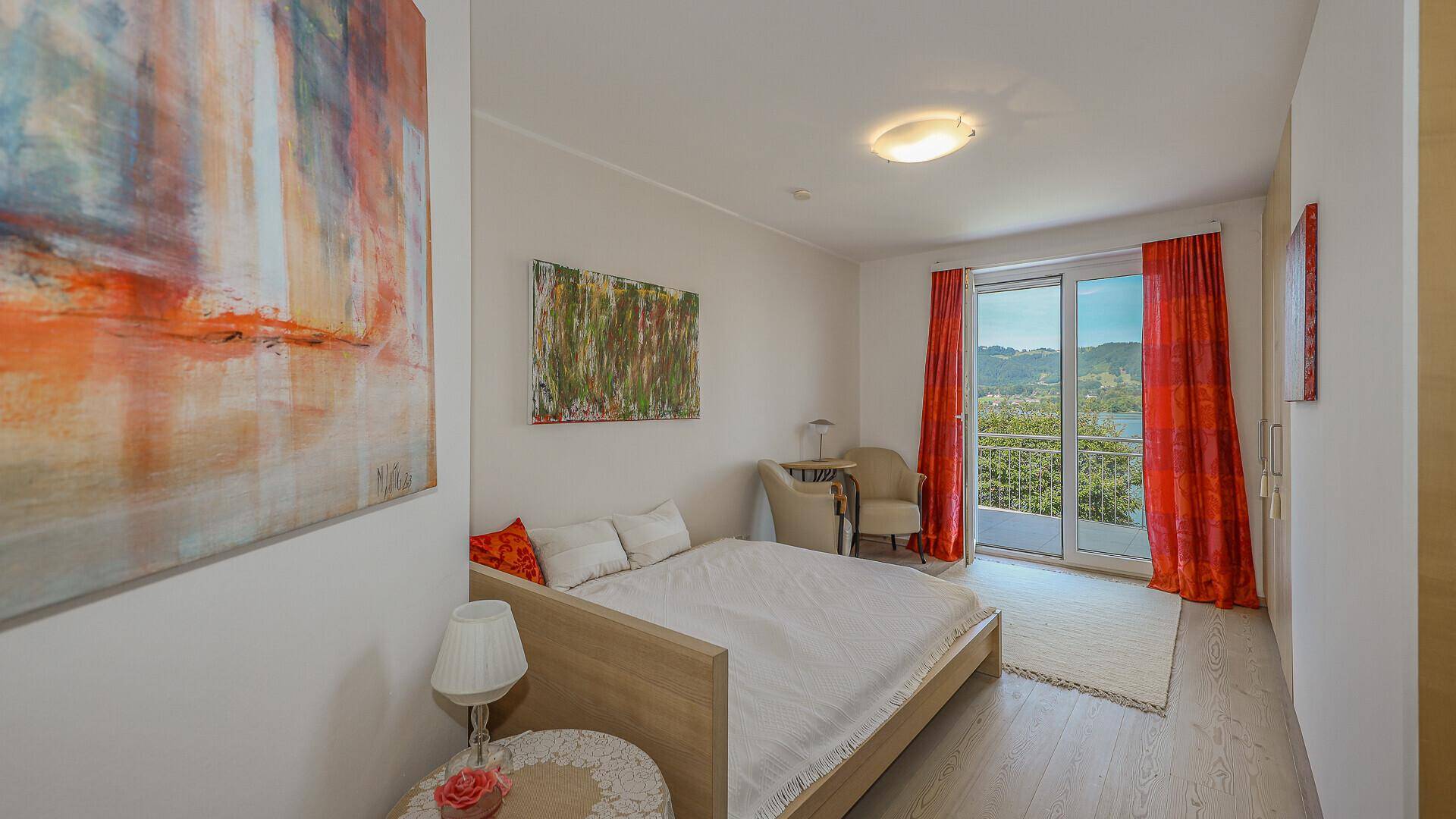 Helles Schlafzimmer mit Doppelbett, Kunstwerken und Zugang zum Balkon mit Seeblick.