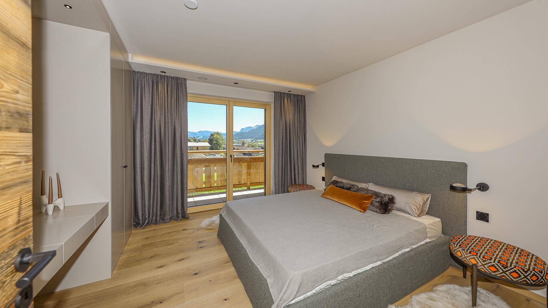 Helles Schlafzimmer mit Doppelbett, Holzboden und Zugang zum Balkon mit Bergblick.