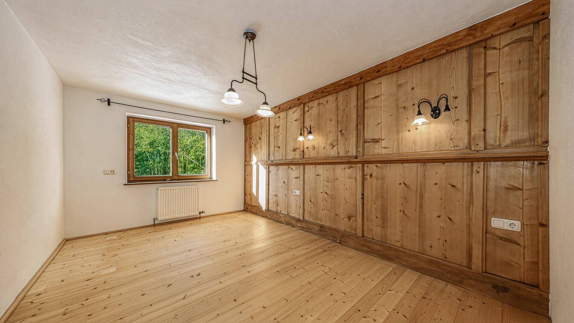 Helles Schlafzimmer mit Holzboden, Holzvertäfelung und Fensterblick ins Grüne.