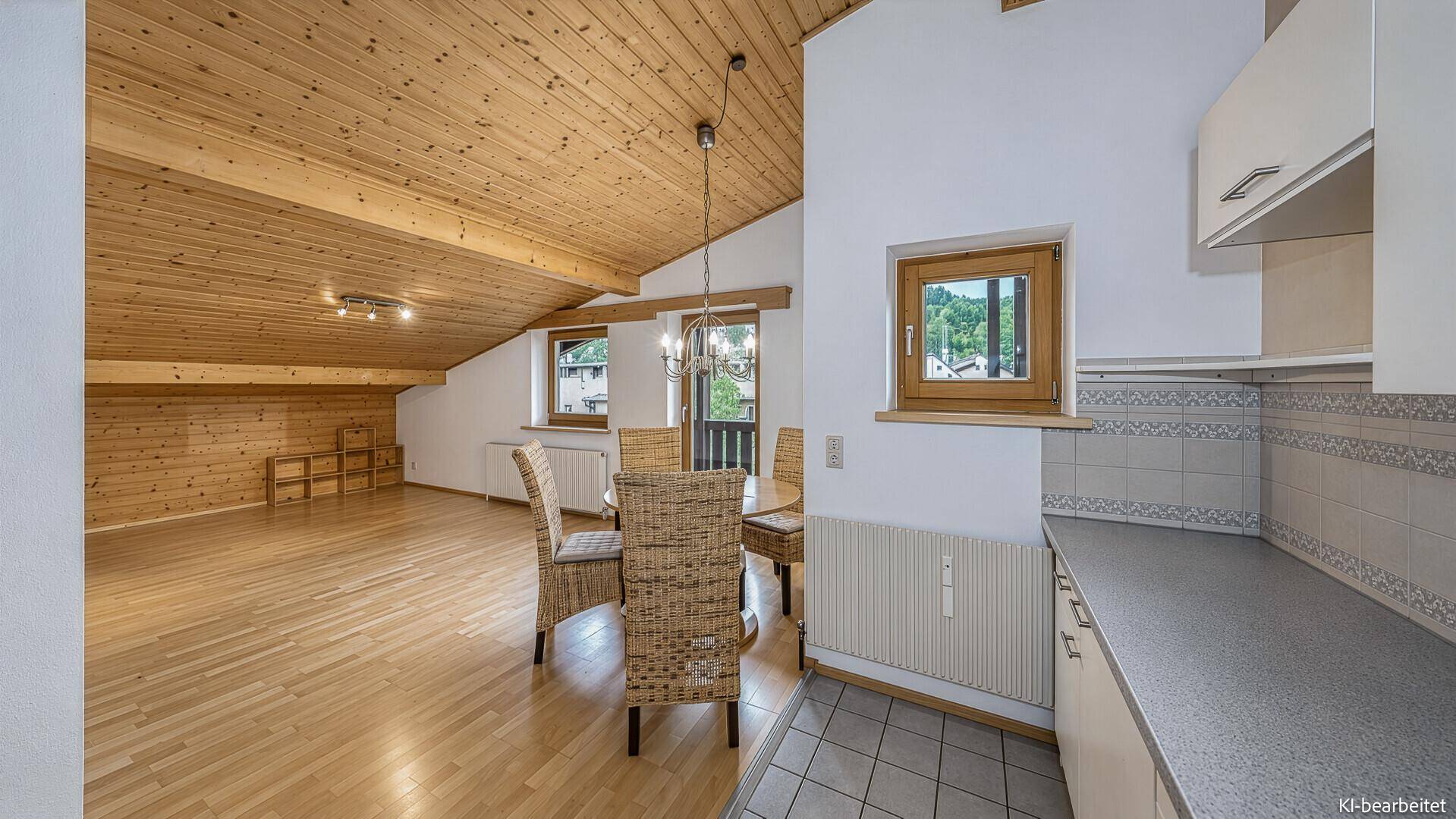 Heller Wohn-Essbereich mit Holzbalkendecke, Parkettboden und kleiner Küchenzeile.