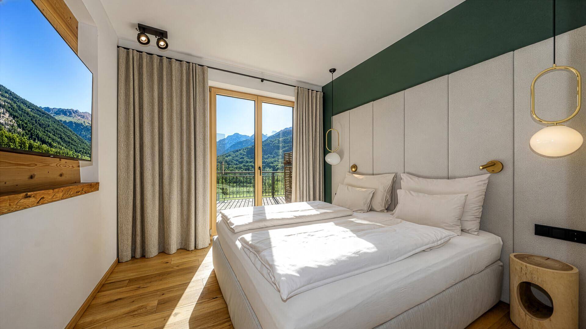 Helles Schlafzimmer mit Doppelbett, Holzboden und direktem Zugang zu einem Balkon mit Bergblick.