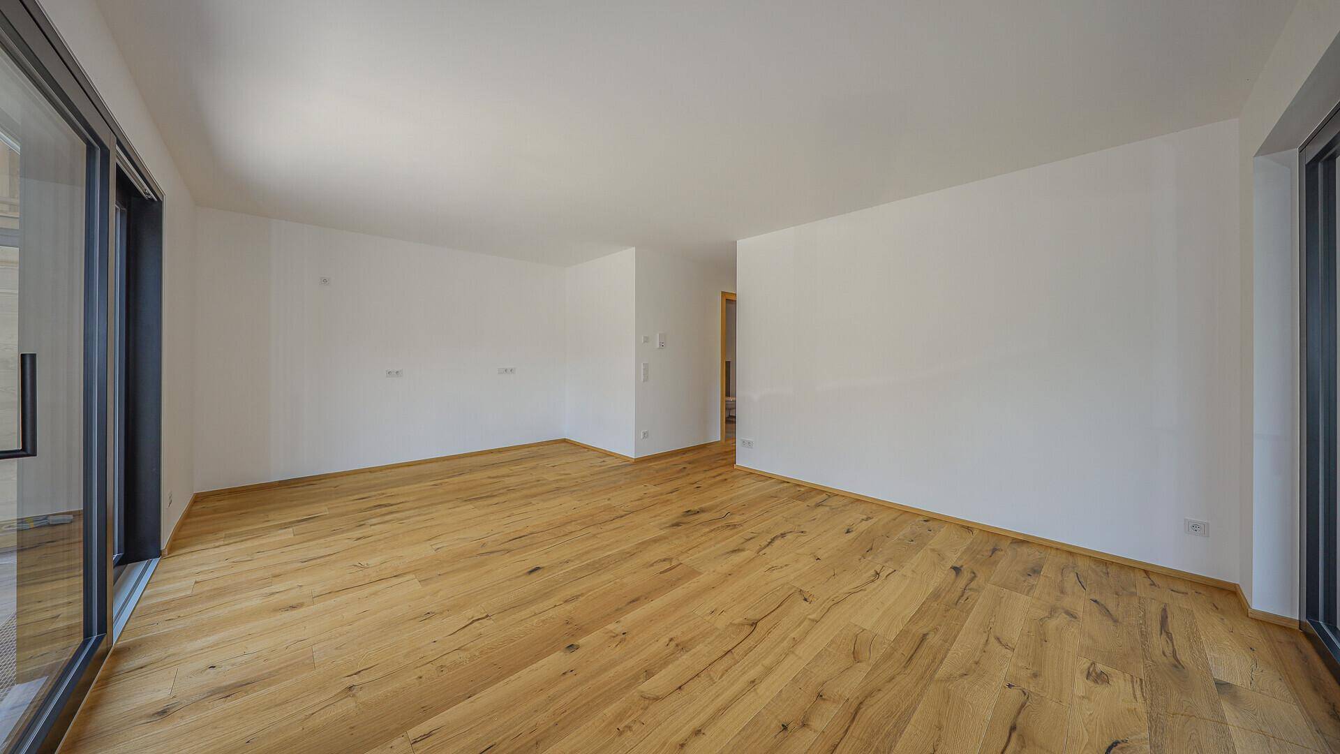 Unmöblierter Wohnbereich mit viel Tageslicht und Holzboden.