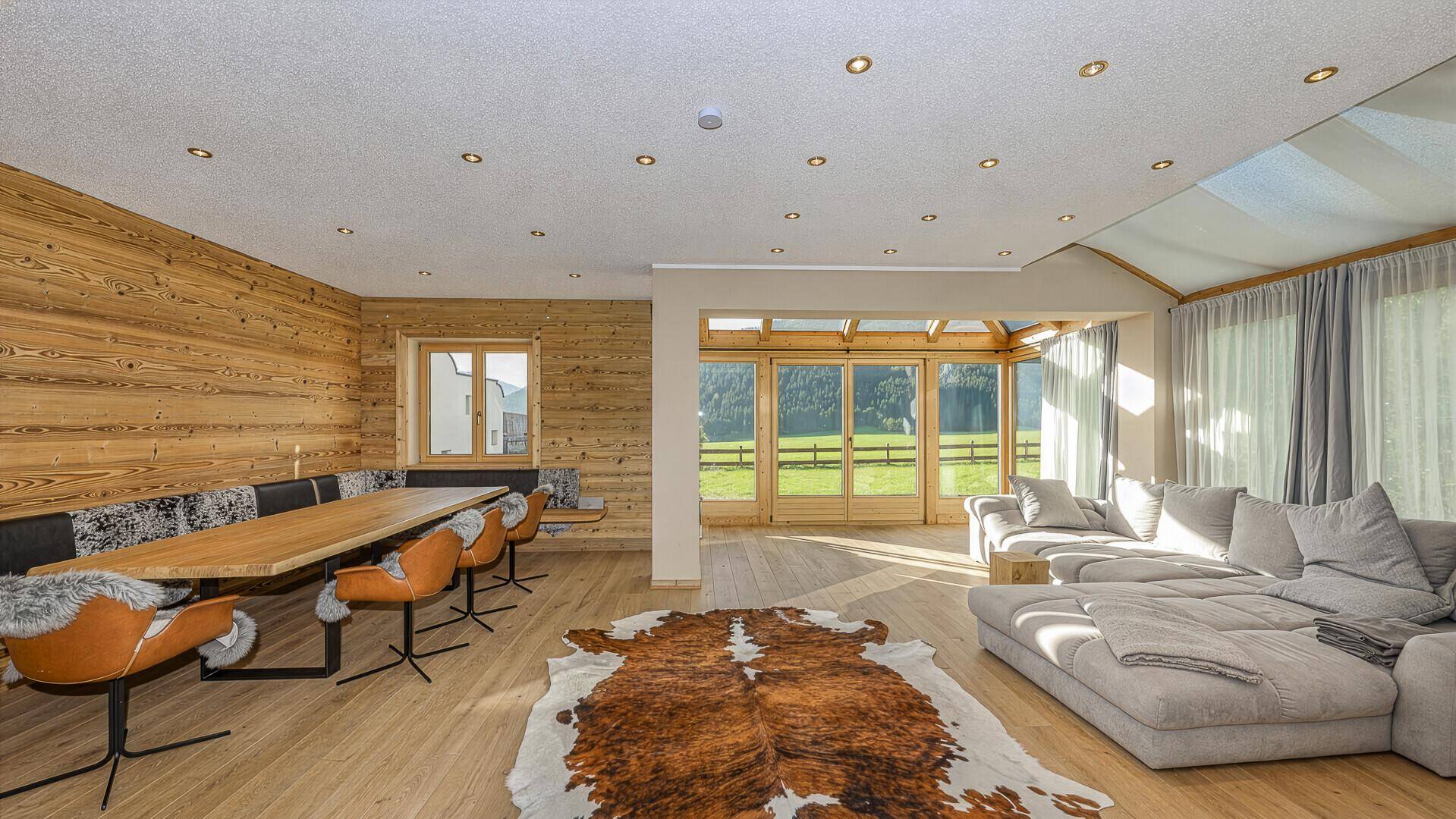Gemütlicher Wohn-Essbereich mit Holzwänden, großem Sofa und Zugang zum lichtdurchfluteten Wintergarten.